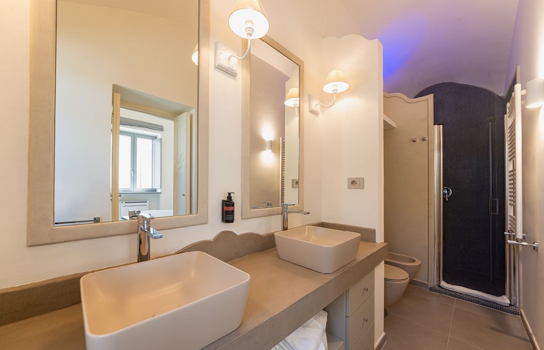 A modern bathroom featuring dual white vessel sinks, a large mirror, and a walk-in shower with black tile accent wall.